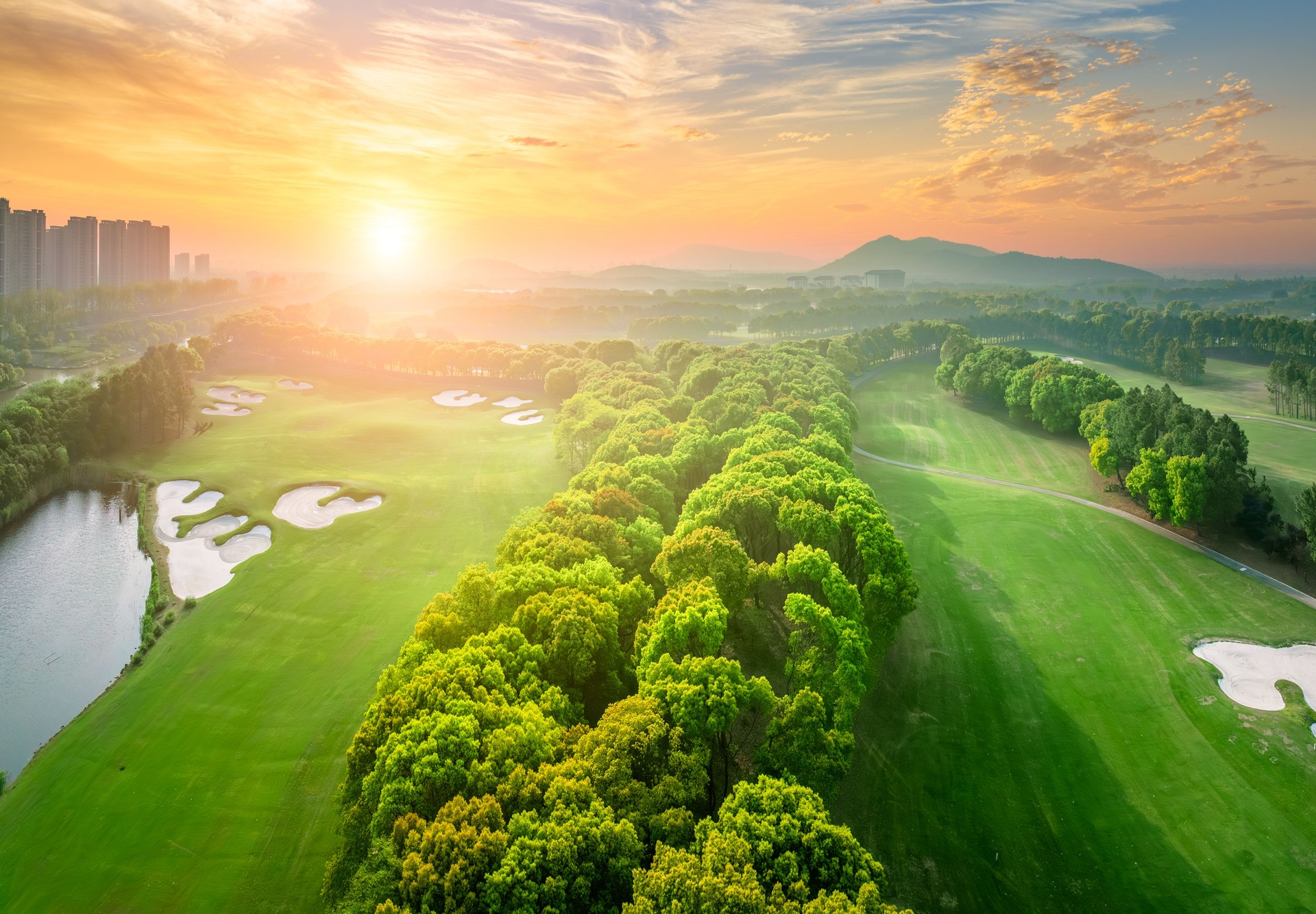 Aerial view of a golf course at sunrise with cityscape in distance